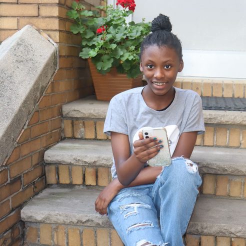 African American Girl smiling holding cell phone sitting on city